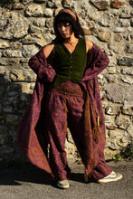 Load image into Gallery viewer, A person stands outdoors against a stone wall wearing a loose bohemian outfit with a dark green vest, wide-leg patterned pants, and a large draped purple patterned shawl or wrap. Buy now online from Emma's Emporium, soft warm fleecy winter hippie hippy trouser pants. Paisley pattern in blue or purple with pockets, unisex baggy trousers for men and women. Shop Emma's Emporium alternative fashion now, for ethical slow fashion, women's funky festival clothing.