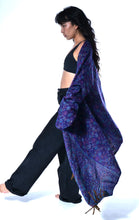 Load image into Gallery viewer, A woman in a black sports bra and wide-leg black pants models a long, open-front shawl or kimono-style wrap in a deep purple and blue paisley pattern against a solid white background. Emma's Emporium paisley fleece blanket cardigan wrap throw. Shop online and buy now ethical slow fashion, unisex, men's, women's boho festival clothing.