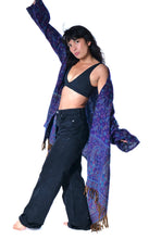 Load image into Gallery viewer, A woman posing in a black bralette and dark wide-leg jeans, draped in a purple and blue paisley patterned shawl with gold fringe, against a solid white background. Emma's Emporium paisley fleece blanket cardigan wrap throw. Shop online and buy now ethical slow fashion, unisex, men's, women's boho festival clothing.