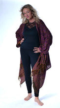 Load image into Gallery viewer, A woman modeling a dark purple and brown patterned shawl with fringe, worn open over a black top and black leggings, against a white studio background. Emma's Emporium paisley fleece blanket cardigan wrap throw. Shop online and buy now ethical slow fashion, unisex, men's, women's boho festival clothing.
