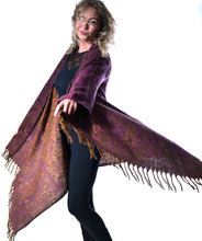 Load image into Gallery viewer, A woman modeling a large patterned shawl with fringe, shown against a plain white background. The shawl has a purple and orange paisley pattern. Emma's Emporium paisley fleece blanket cardigan wrap throw. Shop online and buy now ethical slow fashion, unisex, men's, women's boho festival clothing.