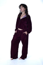 Load image into Gallery viewer, A model wearing a matching deep burgundy velvet lounge set, consisting of a cropped zip-up jacket with a patterned inner collar and wide-leg pants, standing against a white studio background. Buy now online from Emma's Emporium. Baggy unisex velvet jogger trousers with pockets. Emma's Emporium alternative hippie boho winter women's clothing. Alternative fashion, ethical, slow fashion for men and women.
