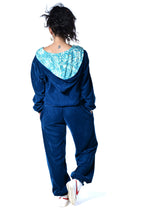 Load image into Gallery viewer, A person shown from the back wearing a dark blue velour tracksuit with a light blue patterned hood lining, paired with white sneakers, on a white background. Buy now online from Emma's Emporium. Baggy unisex velvet trousers with pockets. Emma's Emporium alternative hippie boho winter women's clothing. Alternative fashion, ethical, slow fashion for men and women.
