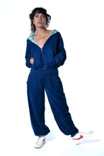 Load image into Gallery viewer, A model wearing a matching navy blue velour tracksuit with a hooded zip-up jacket and wide-leg pants, featuring a light blue patterned inner hood lining, paired with white sneakers. Buy now online from Emma's Emporium. Baggy unisex velvet trousers with pockets. Emma's Emporium alternative hippie boho winter women's clothing. Alternative fashion, ethical, slow fashion for men and women.
