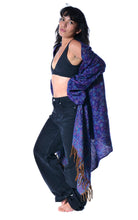 Load image into Gallery viewer, A woman modeling a dark blue and purple patterned shawl draped over her shoulders, paired with a black crop top and dark jeans, against a plain white background. Emma's Emporium paisley fleece blanket cardigan wrap throw. Shop online and buy now ethical slow fashion, unisex, men's, women's boho festival clothing.
