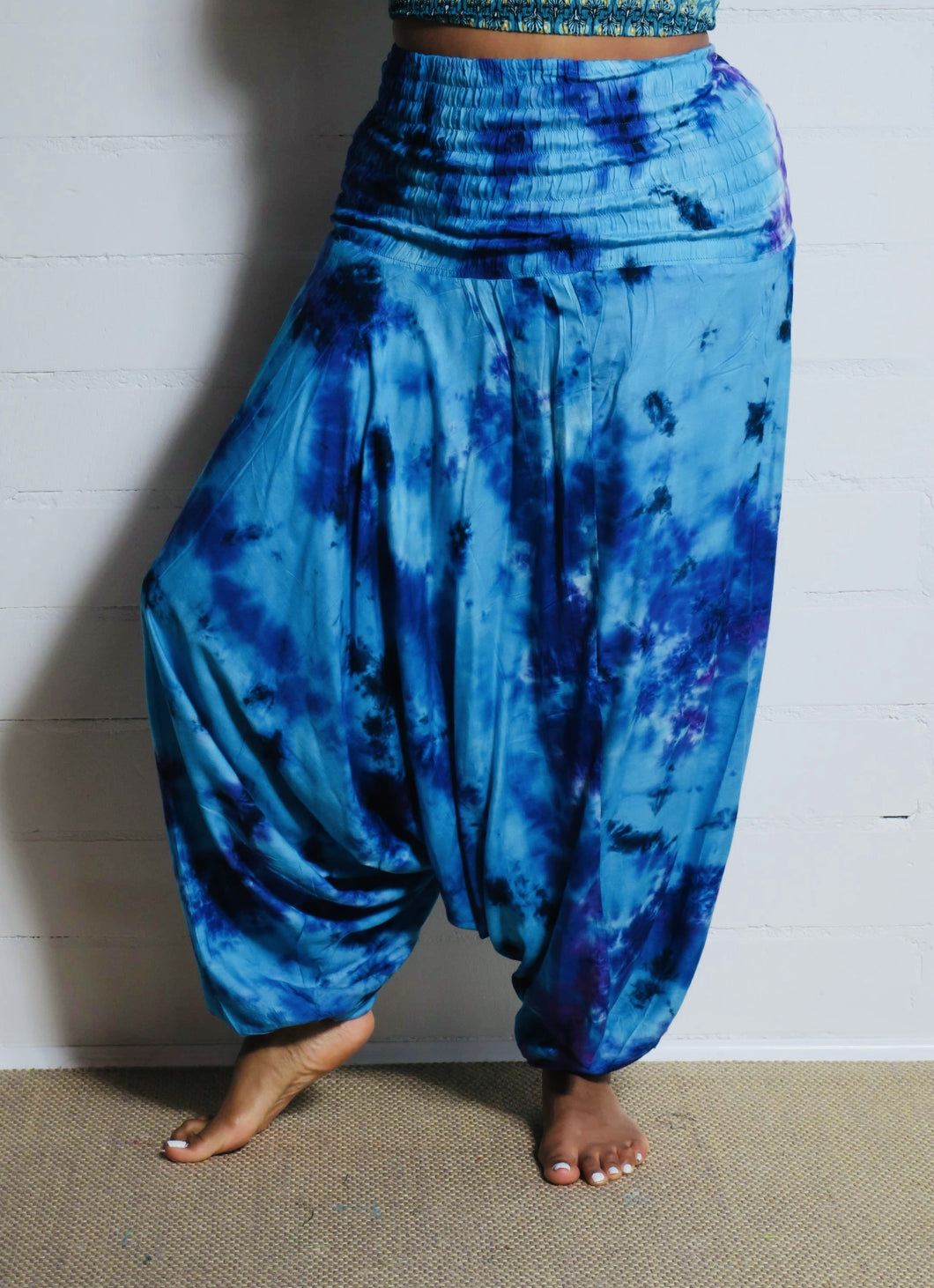 Photo of model in Emma's Emporium tie dye harem trousers, low crotch hippy trousers with wide elastic waistband on bright vibrant tie dye. Made to ethical fair trade standards for Emma's Emporium slow fashion alternative women's clothing. Festival!