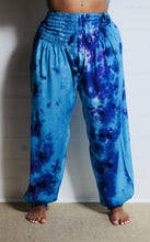 Load image into Gallery viewer, Genie Trousers! Photo of model in Emma&#39;s Emporium tie dye Genie harem trousers, low crotch hippy trousers with wide elastic waistband on bright vibrant tie dye. Made to ethical fair trade standards for Emma&#39;s Emporium slow fashion alternative women&#39;s festival clothing.
