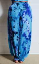 Load image into Gallery viewer, Genie Trousers! Photo of model in Emma&#39;s Emporium tie dye Genie harem trousers, low crotch hippy trousers with wide elastic waistband on bright vibrant tie dye. Made to ethical fair trade standards for Emma&#39;s Emporium slow fashion alternative women&#39;s festival clothing.
